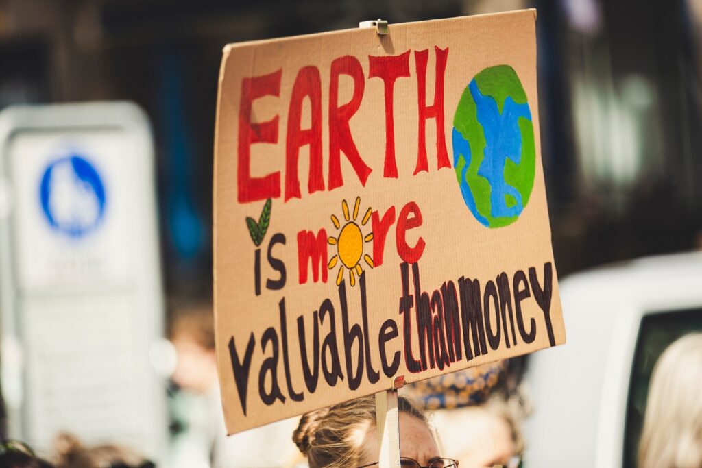 A woman in a crowd holds up a sign that says, “Earth is more valuable than money